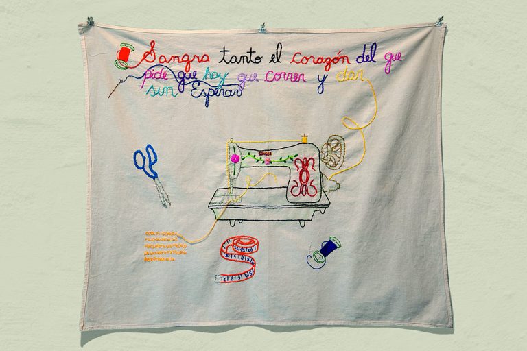 Imagen de un lienzo bordado con la frase: "sangra tanto el corazón del que pide que hay que correr y dar sin esperar" y "evita mi señora muchas gracias por darme los medios de ganarme mi propia independencia", una maquina de coser, una tijera, un centímetro y dos carreteles de hilo.
